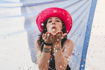 pretty woman with colorful straw hat blowing confetti