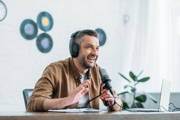 cheerful radio host gesturing while recording podcast in broadcasting studio - obrazy, fototapety, plakaty