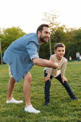 Young man having fun with his little brother or son outoors in park beautiful green grass play game.