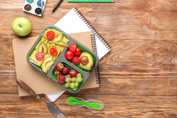 School lunch box with tasty food and stationery on wooden table