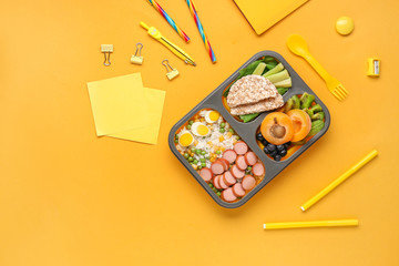 School lunch box with tasty food and stationery on color background