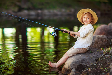 Little curly boy fishing on a lake in a sunny summer day