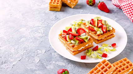 Belgian waffles with fruits strawberries and kiwi on white plate closeup. Tasty healthy breakfast