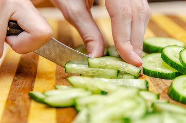 Female hand cuts cucumbers with a knife on the bars on a wooden plank close up