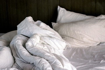 Messy bed. White pillow with blanket on bed unmade. 