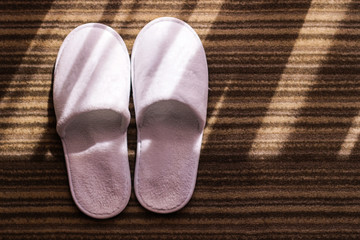 Slippers. White slippers on hotel carpet and sun glares. 