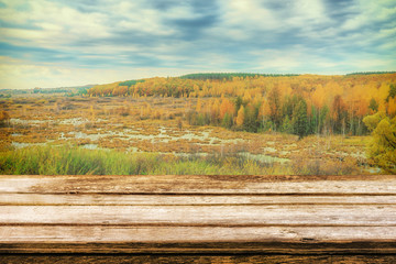 Empty wooden table with picturesque autumn landscape of view from the hill to the lowland with forest and swamps. Mock up for display or montage products