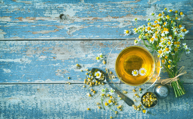 Cup of herbal tea with chamomile flowers on aged blue wood plank