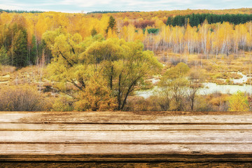 Naklejka na ściany i meble Empty wooden table with picturesque autumn landscape of view from the hill to the lowland with forest and swamps. Mock up for display or montage products