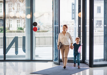 A businesswoman with small daughter entering office building, walking. - obrazy, fototapety, plakaty
