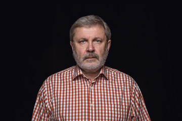 Obraz premium Close up portrait of senior caucasian man isolated on black studio background. Photoshot of real emotions of male model. Standing and looks serious. Facial expression, human nature and emotions