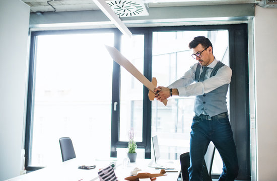 A Young Businessman With Sword In An Office, Having Fun. A Competition Concept.