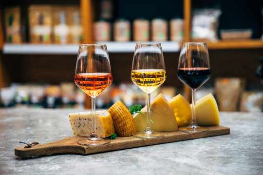 Glasses of Wine and cheese. Assortment or various type of cheese and wine glasses on the table in restaurant. Red, rose and yellow wine or champagne on the table. Winery concept image