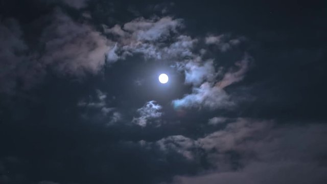 Full Moon Moves in the Night Sky through Dark Clouds. Time lapse. The mystical moon rises up. Moonlight Shines in the black night sky. Two stars in the night sky against the backdrop of the moon and