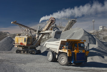 Heavy truck, excavator and rock stone crushing plant against the blue sky in sunny weather. Mining industry. Quarry mining equipment.