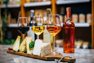 Glasses of Wine and cheese. Assortment or various type of cheese, wine glasses and bottles on the table in restaurant. Red, rose and yellow wine or champagne on the table. Winery concept image