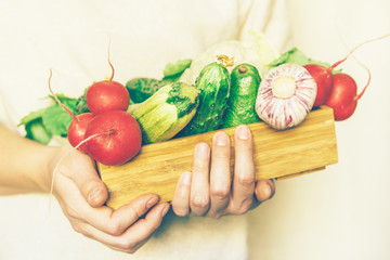 Close up of female hands holding wooden box with seasonal crop of vegetables, vegan set, healthy...