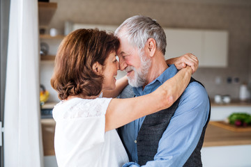 Affectionate senior couple in love standing indoors at home, hugging.