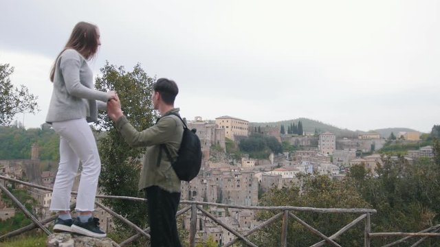 Young couple stand on observation deck holding hands on the background of the ancient town