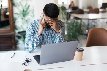 Portrait of an Indian male frustrated with work sitting in front of a laptop in modern office