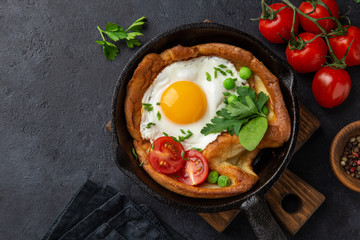 Savory Dutch baby pancake with fried egg, tomato and green peas in cast iron pan