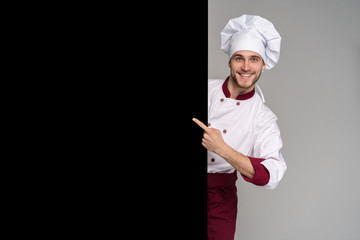 Image of smiling young cook in uniform standing isolated over grey wall background. Looking camera...