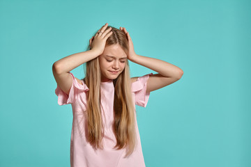 Fototapeta premium Studio portrait of a beautiful girl blonde teenager in a pink t-shirt posing over a blue background.