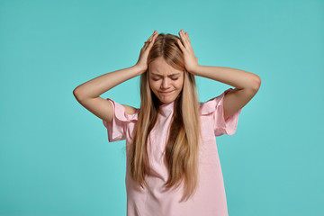 Fototapeta premium Studio portrait of a beautiful girl blonde teenager in a pink t-shirt posing over a blue background.