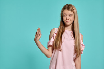 Fototapeta premium Studio portrait of a beautiful girl blonde teenager in a pink t-shirt posing over a blue background.