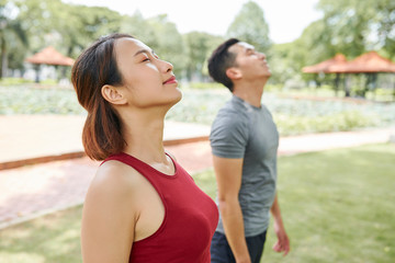 Obraz premium Smiling calm young Asian woman inhaling fresh air and preparing for outdoor training
