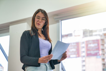 Young woman reading paper in the office making grimaces