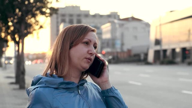 Woman making phone calls on the street. Middle-aged woman talking on a smartphone on the street, cars are passing nearby