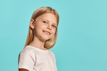 Close-up studio shot of a lovely blonde little girl in a white t-shirt posing against a blue background.