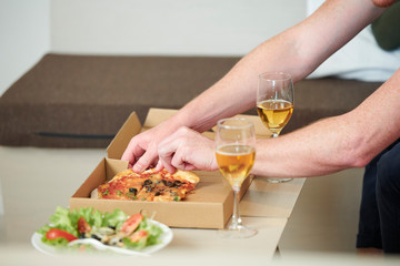 Hands of man taking slice of pizza from the box on small table at home