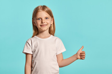 Close-up studio shot of a lovely blonde little girl in a white t-shirt posing against a blue background.