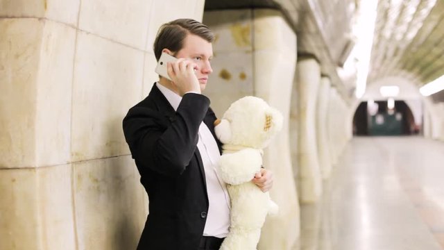Man talking on the phone with his beloved, in his hand a gift is a toy bear.