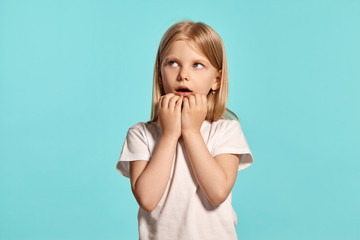 Close-up studio shot of a lovely blonde little girl in a white t-shirt posing against a blue background.