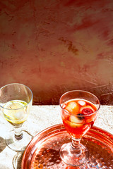 Glasses of aperol spritz and white wine with ice and fruits on sand background outdoors
