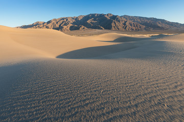 Early Morning Sunlight Over Sand Dunes And Mountains At  Mesquite flat dunes, Death Valley National...