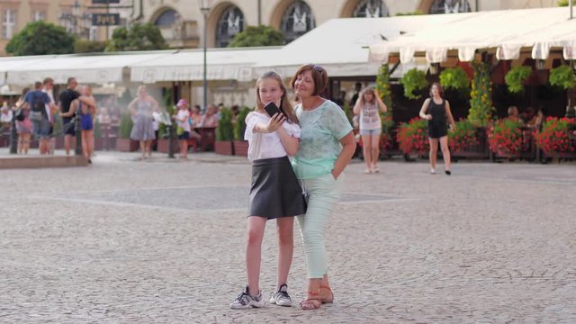 Teenager granddaughter girl have funny time with grandmother taking phone selfie picture in a city