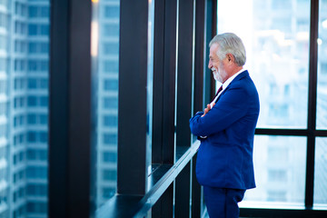 Mature businessman looking out of a window at the city skyline from an office building
