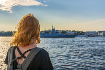 Redhead tween tourist girl on Neva river embankment looking at warships and architectural ensemble in summer evening at sunset. Authentic lifestyle moments, travel concept. Saint Petersburg, Russia