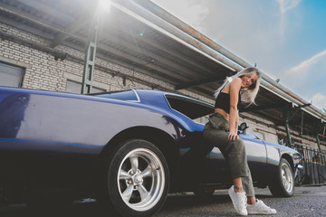 Beautiful Caucasian female posing with an old classic retro muscle car. Automotive lifestyle