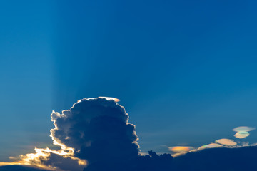 Cloud iridescence on blue sky with sunbeam.