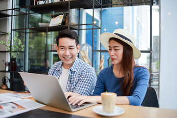 Asian couple in blue shirt drinking coffee talking and working with computer laptop smile and  happy mood in coffee shop cafe