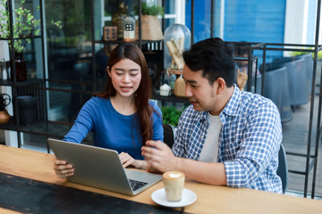 Asian couple in blue shirt drinking coffee talking and working with computer laptop smile and  happy mood in coffee shop cafe © chayathon2000