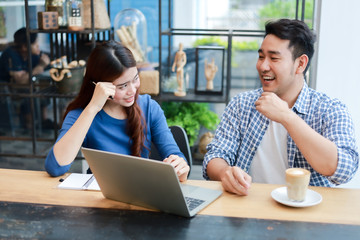 Asian couple in blue shirt drinking coffee talking and working with computer laptop smile and  happy mood in coffee shop cafe