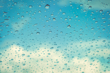 Rain drops, water drops of rain on a window glass. blurred lights city with sky clouds in rainy day, abstract blue background texture, view beautiful from outside window