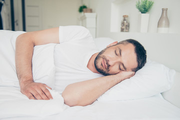 Close up side profile photo fall asleep he him his attractive guy vacation sunday saturday daily dream eyes closed lean head arm hand white nightwear sleep wear t-shirt lying bed bright room indoors