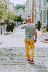 Gray-haired mature man walking along the street in city